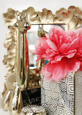 An accent piece next to a mirror and flower arrangement.
